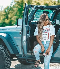 a woman sitting in the back of a blue jeep with her feet up on the door