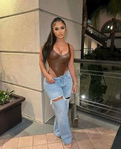 a woman in ripped jeans and a brown top posing for the camera with her hands on her hips