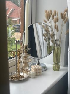 a mirror and some candles are on a window sill near a vase with dry grass