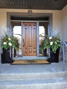 two planters with white flowers are on the front step of a house that is decorated with metal handrails