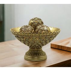 an ornately decorated gold bowl on a wooden table next to a vase with two birds in it