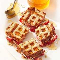 four waffle sandwiches on a white plate with syrup and honey in the background for garnish