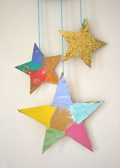 three colorful stars hanging from strings against a white wall with gold glitter paint on them