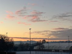 the sun is setting over a tennis court with lights on and snow covering the ground