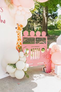 a giraffe standing next to a pink jeep with balloons in the shape of animals