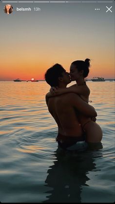 two people sitting in the water at sunset, one is kissing the other's cheek