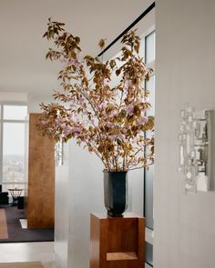 a vase filled with pink flowers sitting on top of a wooden stand next to a window