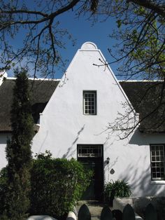 a white house with a black door and windows on the side of it, surrounded by greenery