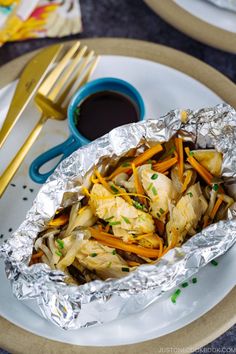 chicken and carrots wrapped in tin foil on a plate next to a cup of coffee