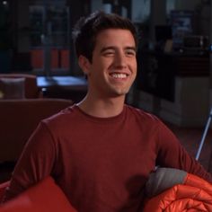 a young man smiling while sitting in a chair with an orange blanket on his lap