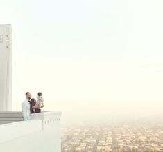 a man and woman sitting on the edge of a building with a baby in their lap