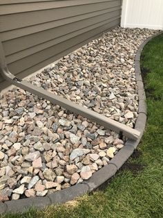 a rock garden bed in front of a house with grass on the ground and rocks around it