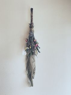 a piece of driftwood hanging on the wall with flowers and feathers attached to it