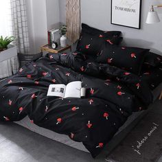 a bed with black sheets and red flowers on it, next to an open book