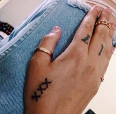 a person with a cross tattoo on their left hand holding onto another persons arm and wearing gold rings