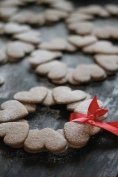 heart shaped cookies tied with a red ribbon on top of a wooden table in the shape of a wreath