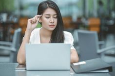 a woman sitting at a table with a laptop in front of her and looking down