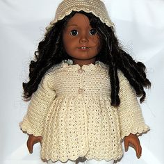 a doll wearing a white knitted dress and bonnet with braids on her head