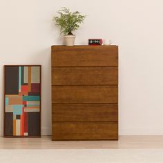 a wooden dresser sitting next to a plant on top of a hard wood floor in front of a white wall