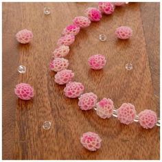 pink flowers are arranged in the shape of a heart on a wooden table with clear beads