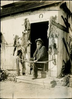 black and white photograph of two men standing in front of a door with horses behind them