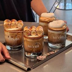 three glasses filled with different types of desserts on a tray in front of a person