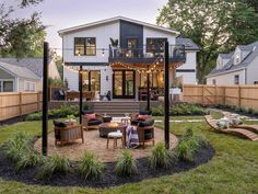 an outdoor patio with seating and fire pit in front of a house at dusk, surrounded by greenery