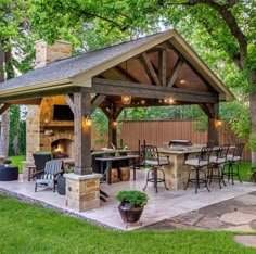 a covered patio with an outdoor kitchen and grill in the back yard, surrounded by trees