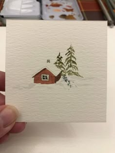 a hand holding up a card with a house and trees on it