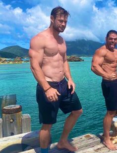 two men standing on a dock next to each other with their bare chests and no shirts