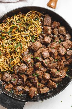 meat and noodles in a skillet on a white table with utensils next to it