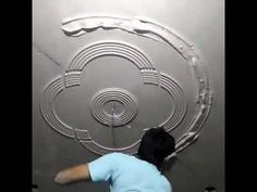 a man in blue shirt and black pants painting a metal wall with circles on it