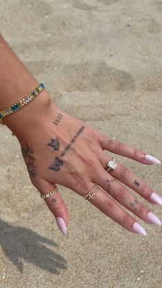 a woman's hand with tattoos and bracelets on her left wrist, in the sand