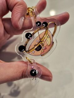 a hand holding two keychains with black and white designs on them, one in the shape of a teapot