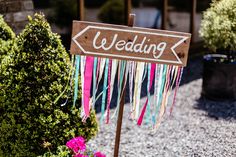 a wooden sign that says wedding with streamers hanging from it's sides in front of potted plants