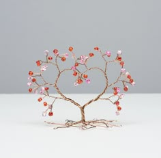 a wire tree sculpture with pink and red beads on it's branches, against a gray background