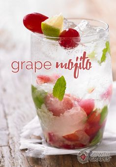 a glass filled with ice and fruit on top of a wooden table next to a napkin