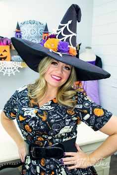 a woman wearing a witches hat and smiling at the camera while standing in front of halloween decorations