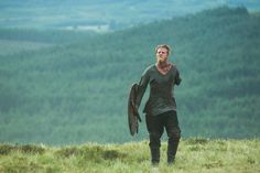 a man holding a bird on top of a lush green hillside