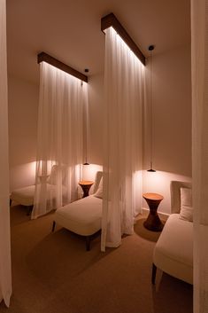 a room with three beds and two lamps on either side of the bed are white drapes hanging from the ceiling