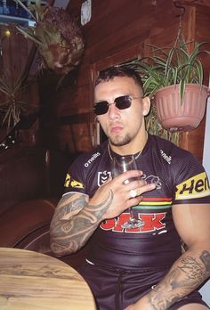 a man sitting at a table with a glass in his hand and tattoos on his arm