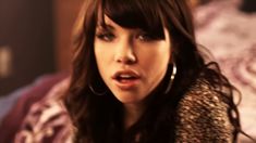 a close up of a person sitting on a bed with her mouth open and wearing large hoop earrings