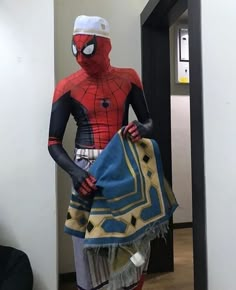 a man in a spiderman costume is standing next to a door and holding a blanket