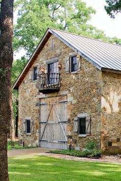 an old stone building with wooden doors and windows on the front porch is surrounded by trees