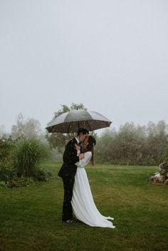 a bride and groom kissing under an umbrella in the rain outside on their wedding day