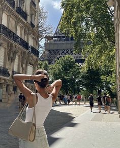 a woman in white shirt and jeans walking down street next to building with eiffel tower in background