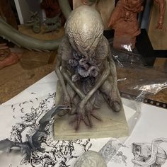 an alien figurine sitting on top of a table next to other statues and artwork