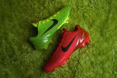 two soccer cleats are laying on the green grass, one is red and the other is green