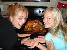 two women standing next to each other in front of an oven with a turkey on it