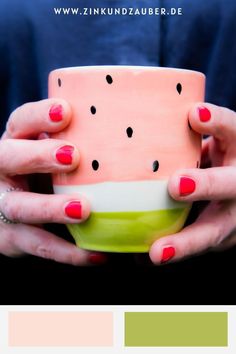 a woman holding a cup with watermelon painted on it and the colors in her hands